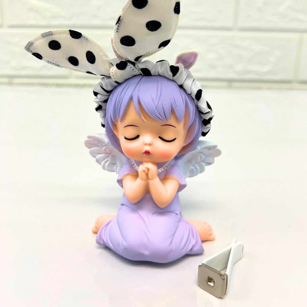 Purple-haired angel figurine with polka dot bunny ears, sitting in a peaceful pose with a metal clip accessory beside it