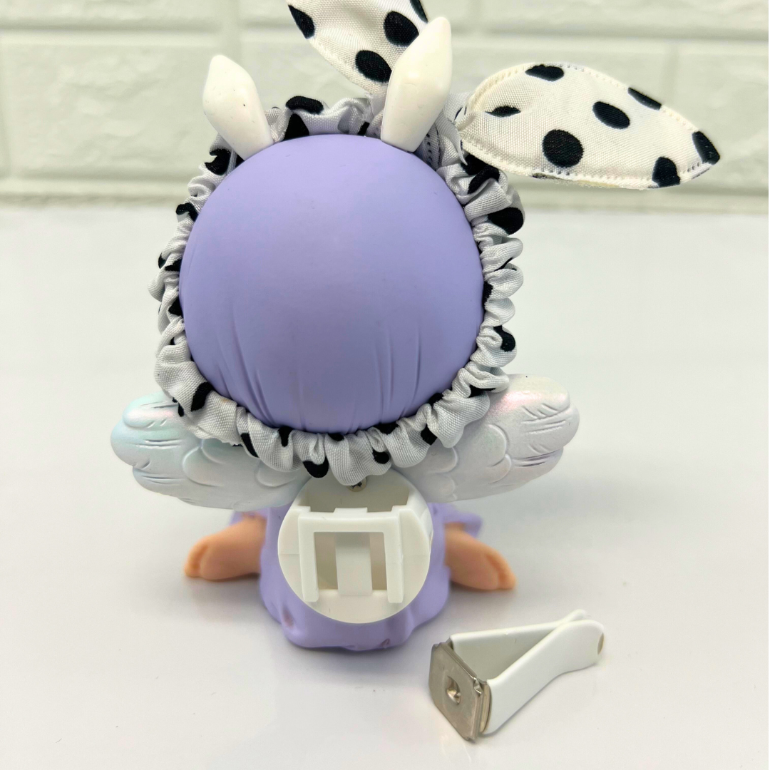 Back view of a purple-haired angel figurine with polka dot bunny ears, showing the attachment mechanism and a metal clip accessory beside it.