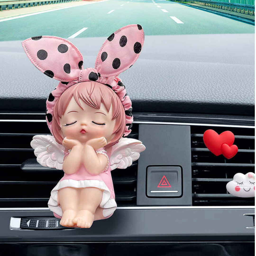 Pink-haired angel figurine with polka dot bunny ears, sitting on a car dashboard, adding a cute and calming touch to the interior.