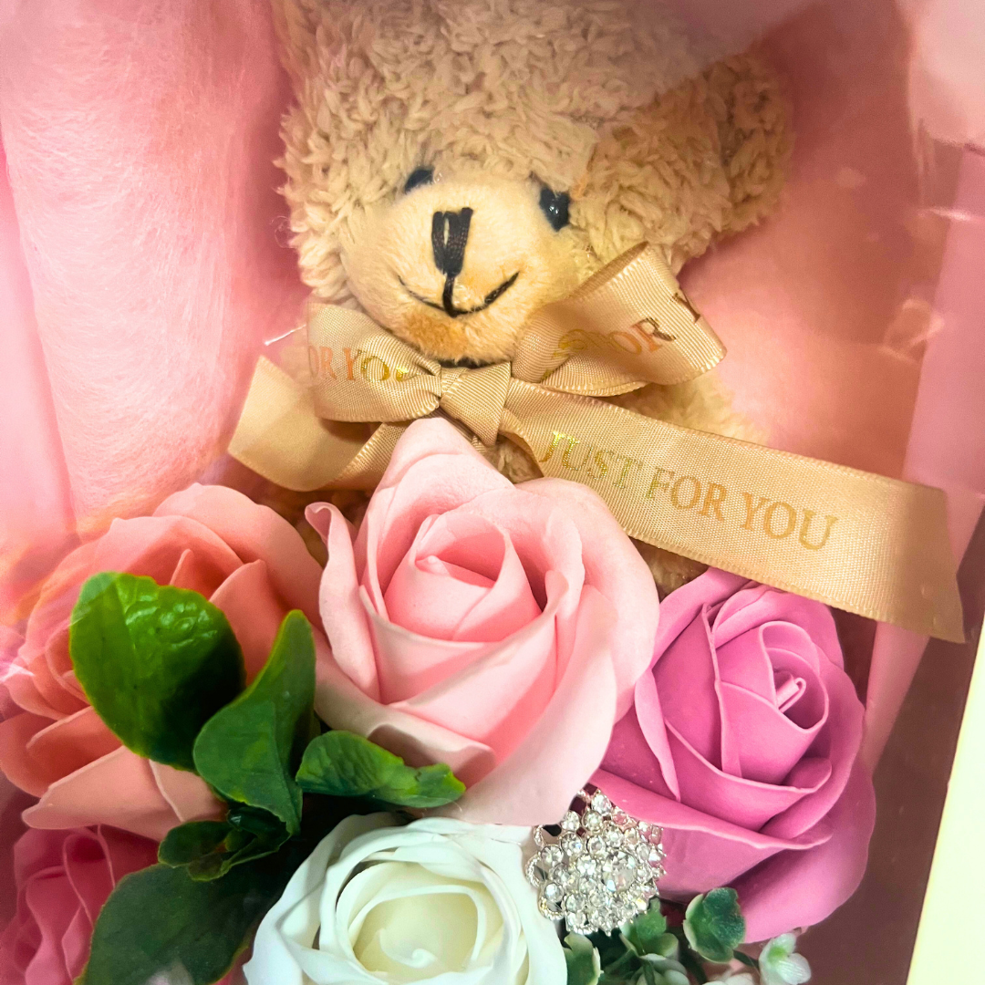 Close-up of a teddy bear with a gold ribbon among pink and white soap flowers.