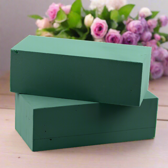 Two wet floral foam blocks stacked on a table with roses in the background.