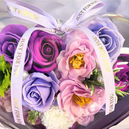 Purple and pink soap flowers arranged in a heart-shaped bouquet, tied with a lavender ribbon.